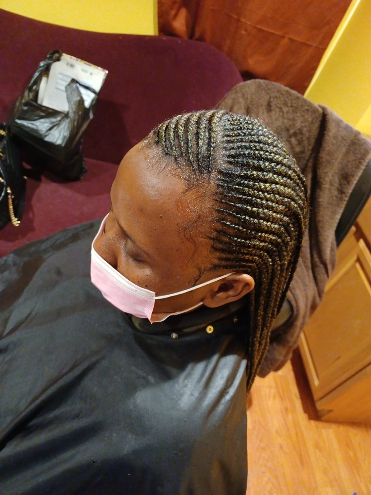 Woman wearing a face mask getting her hair braided into cornrows
